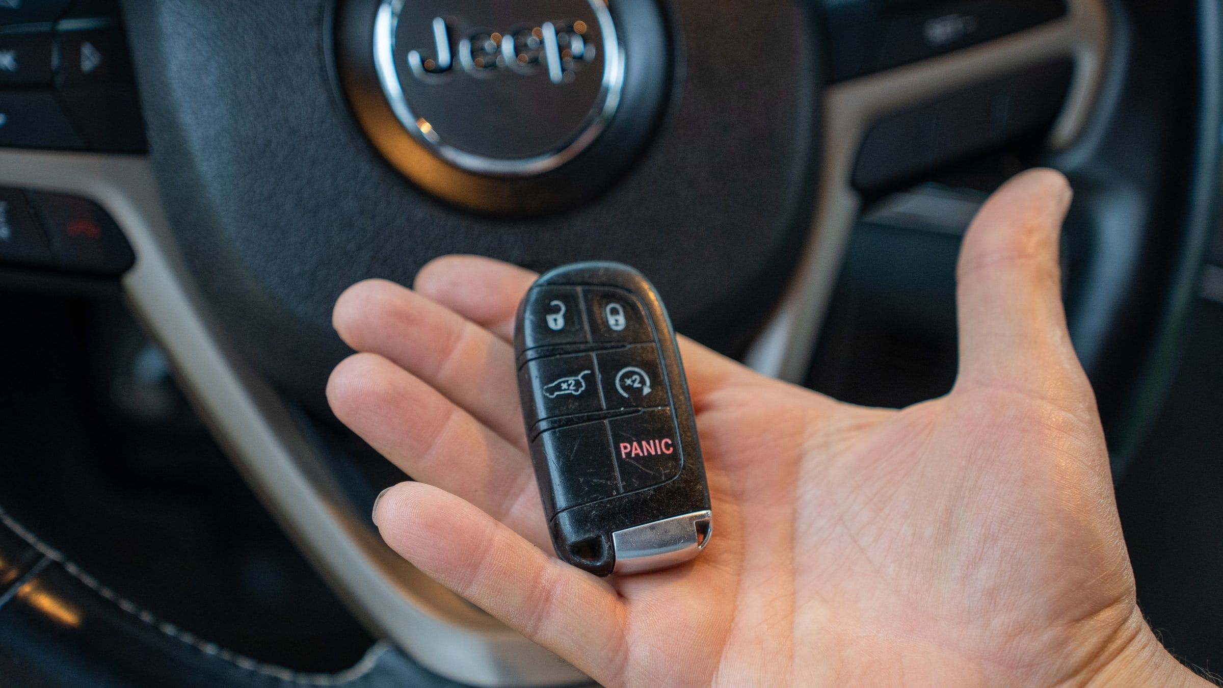 A car key fob resting in an open palm in front of a steering wheel.